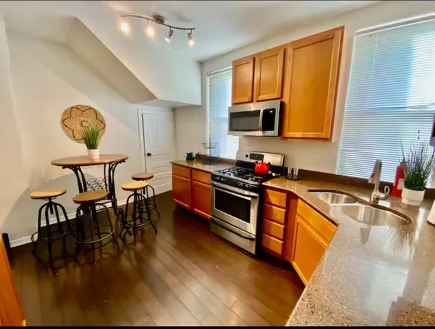 a kitchen with stainless steel appliances granite countertop a stove top oven a sink a dining table and chairs with wooden floor