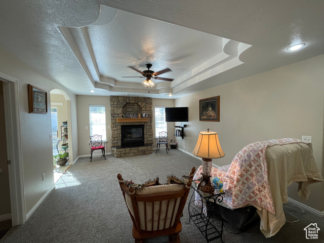 11473 South Dempsey Creek Road Lava Hot Springs, ID 83246 - Photo 6 of 47 Carpeted living area with arched walkways, a stone fireplace, a raised ceiling, a textured ceiling, and ceiling fan