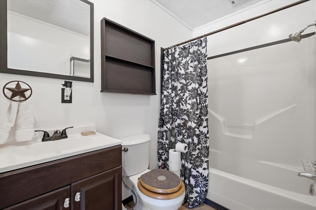 237 Brenda Lane Gainesville, TX 76240 - Photo 16 of 40 Bathroom featuring a white vanity with a dark wood-finish cabinet and a bronze-finish faucet, a white toilet with a wood-finish seat, a white tub and shower combination, a dark wood-finish framed mirror, and a dark wood-finish wall shelf