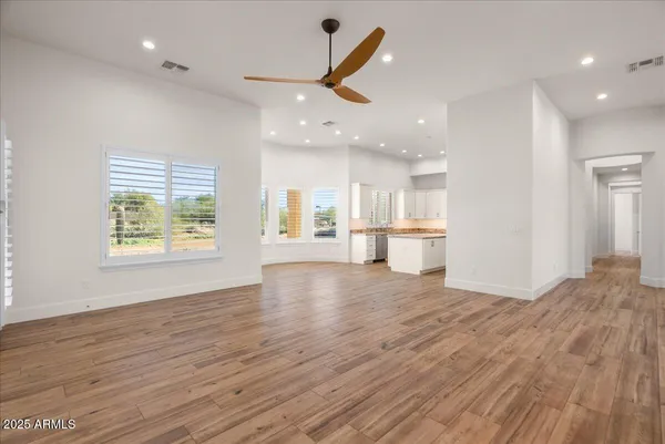 a view of an empty room and kitchen with wooden floor and windows
