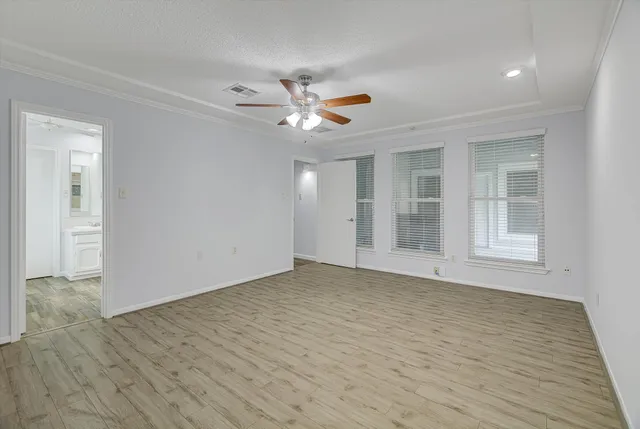 a view of an empty room with wooden floor and a ceiling fan