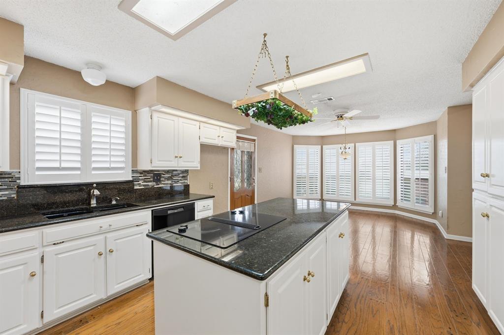 7260 Hudson Cemetery Road Mansfield, TX 76063 - Photo 20 of 40 Kitchen featuring a central island with an integrated cooktop, dark stone countertops, white cabinetry, wood-finish flooring, and a bay window area with plantation shutters