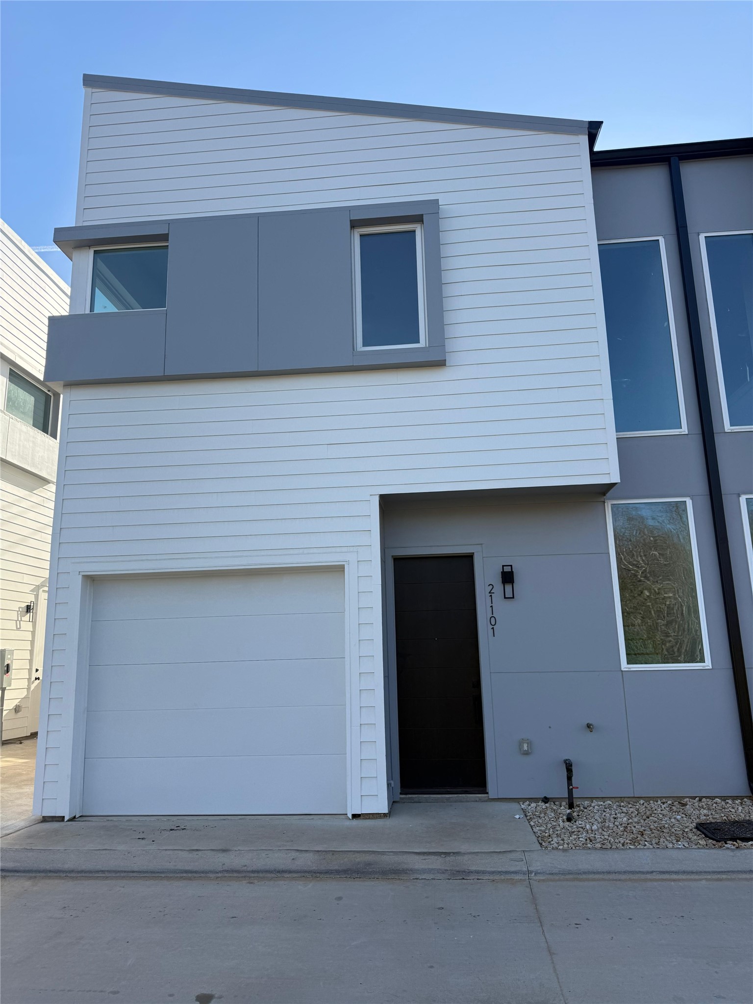 2000 Riverside Farms Road, Unit 10102 Austin, TX 78741 - Photo 10 of 10 Modern townhouse with a sleek facade featuring a mix of white and gray panels. Includes a single-car garage and a tall, narrow window next to the entrance, creating a contemporary look.