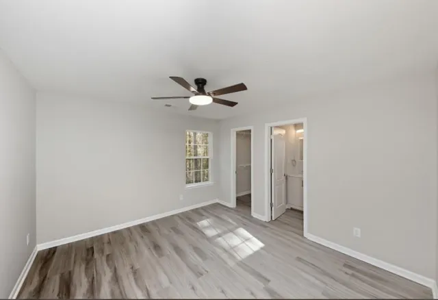 an empty room with wooden floor chandelier fan and windows