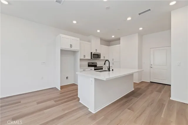 a large white kitchen with wooden floor and stainless steel appliances