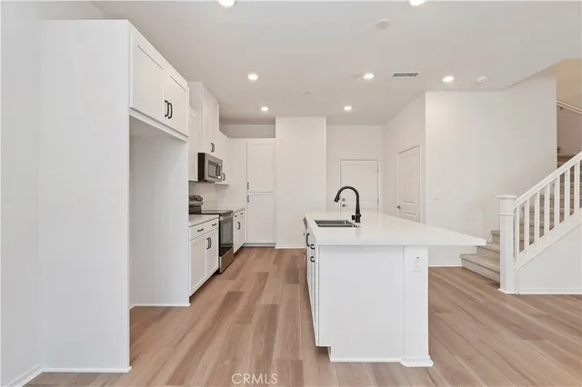 a view of a kitchen with kitchen island a sink wooden floor and stainless steel appliances