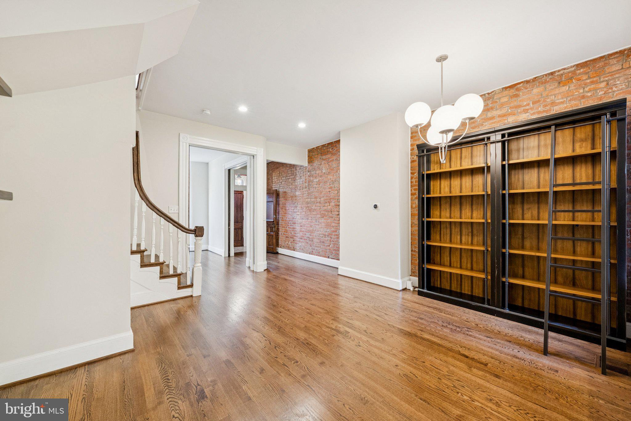 a view of an empty room with wooden floor staircase and a kitchen