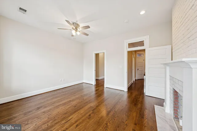 a view of an empty room with wooden floor and a ceiling fan