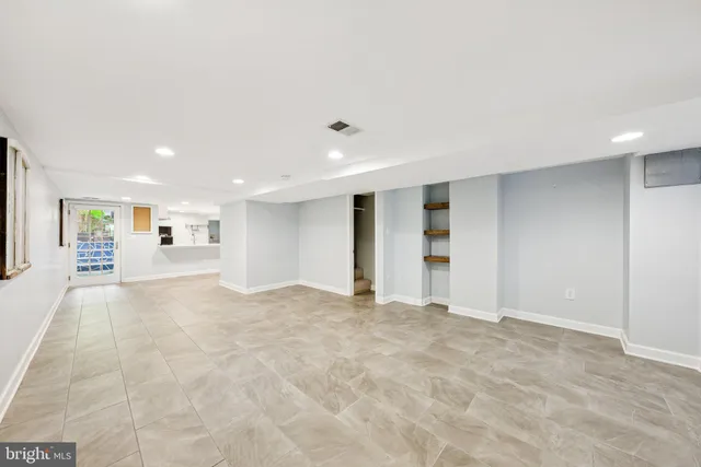 a view of an empty room with kitchen and window