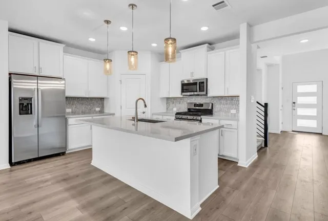 a kitchen with kitchen island granite countertop a refrigerator a sink a stove a microwave and wooden floor