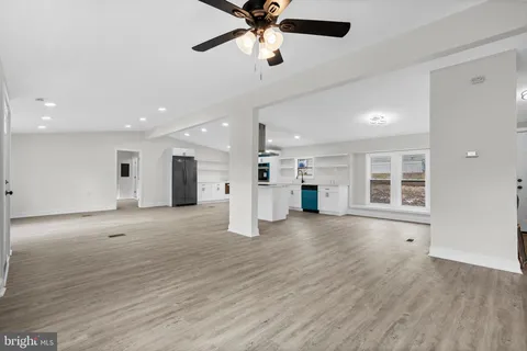 an empty room with wooden floor a ceiling fan a kitchen view and a window