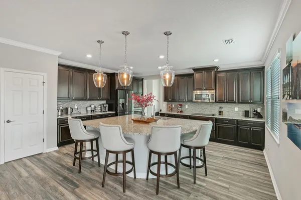 a kitchen with stainless steel appliances kitchen island granite countertop a kitchen island a stove a refrigerator a sink a dining table and chairs with wooden floor