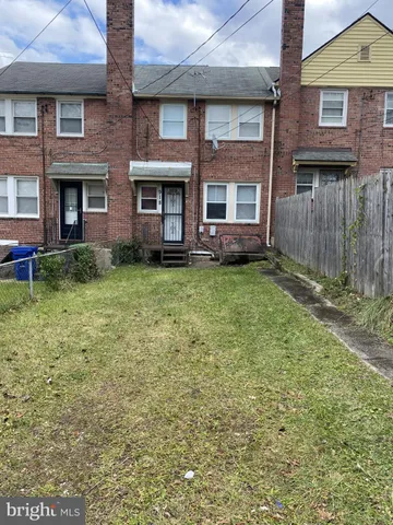 a view of a brick house with a yard plants and large tree