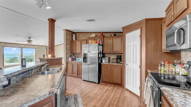 a kitchen with stainless steel appliances granite countertop a refrigerator a stove top oven a sink island and couches with wooden floor