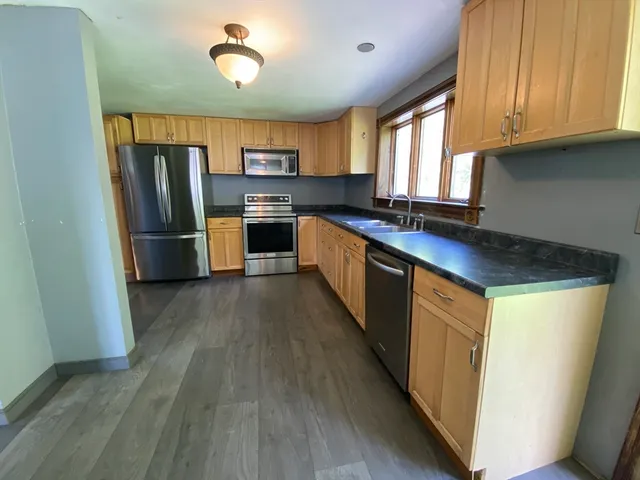 a kitchen with stainless steel appliances granite countertop a refrigerator a sink dishwasher a stove and white countertops with wooden floor