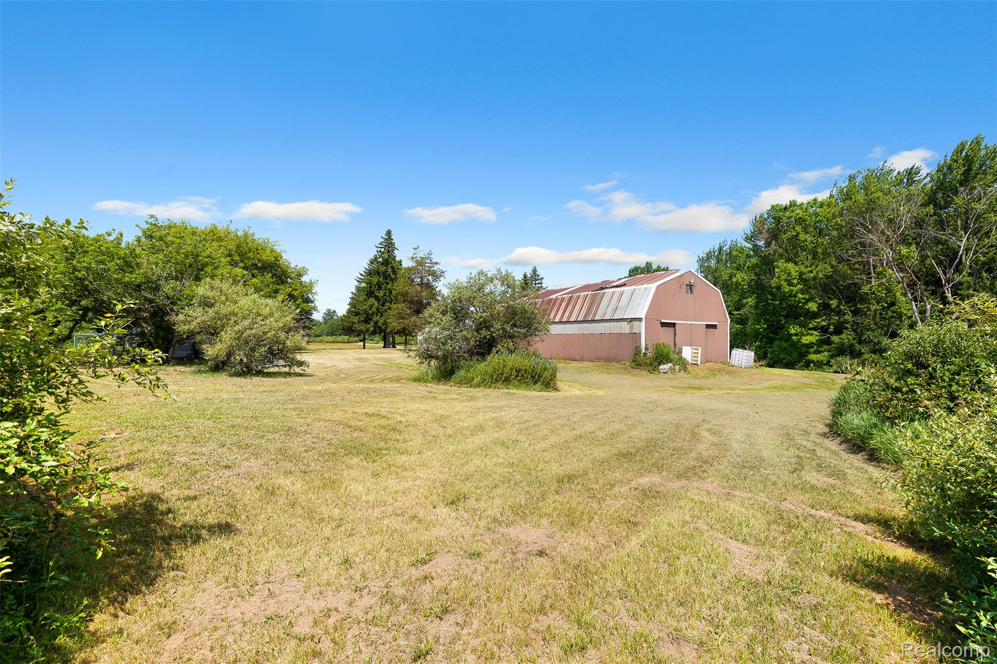 27901 Brandes Road Flat Rock, MI 48134 - Photo 28 of 38 Large agricultural structure with a metal gambrel roof and red siding, surrounded by expansive grassy areas and mature trees