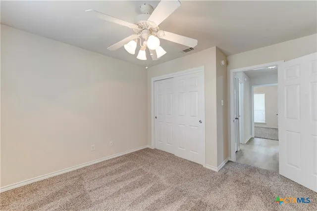 an empty room with a chandelier fan and wooden floor
