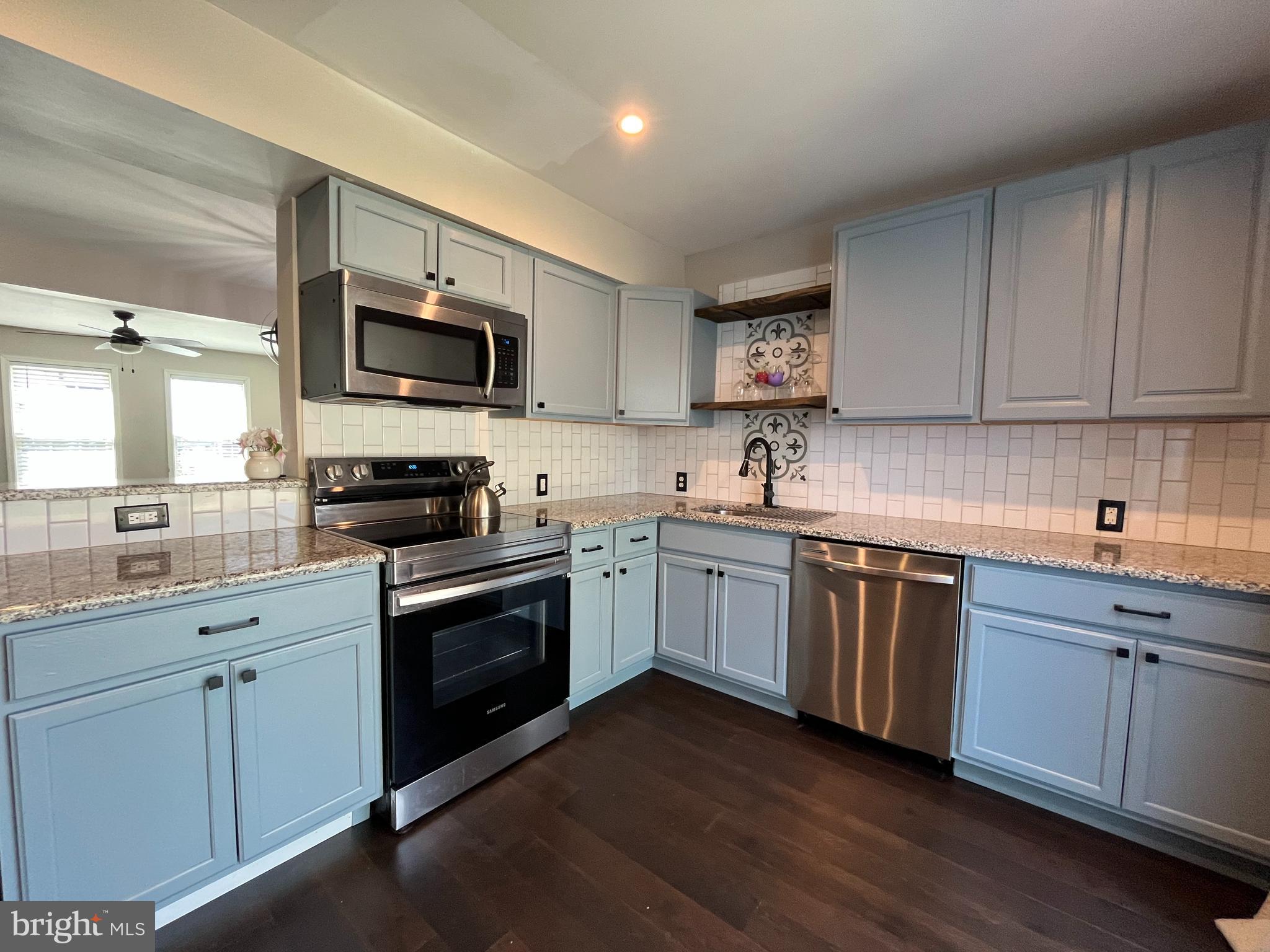 a kitchen with stainless steel appliances granite countertop a sink dishwasher a stove top oven a refrigerator with grey cabinets and wooden floor