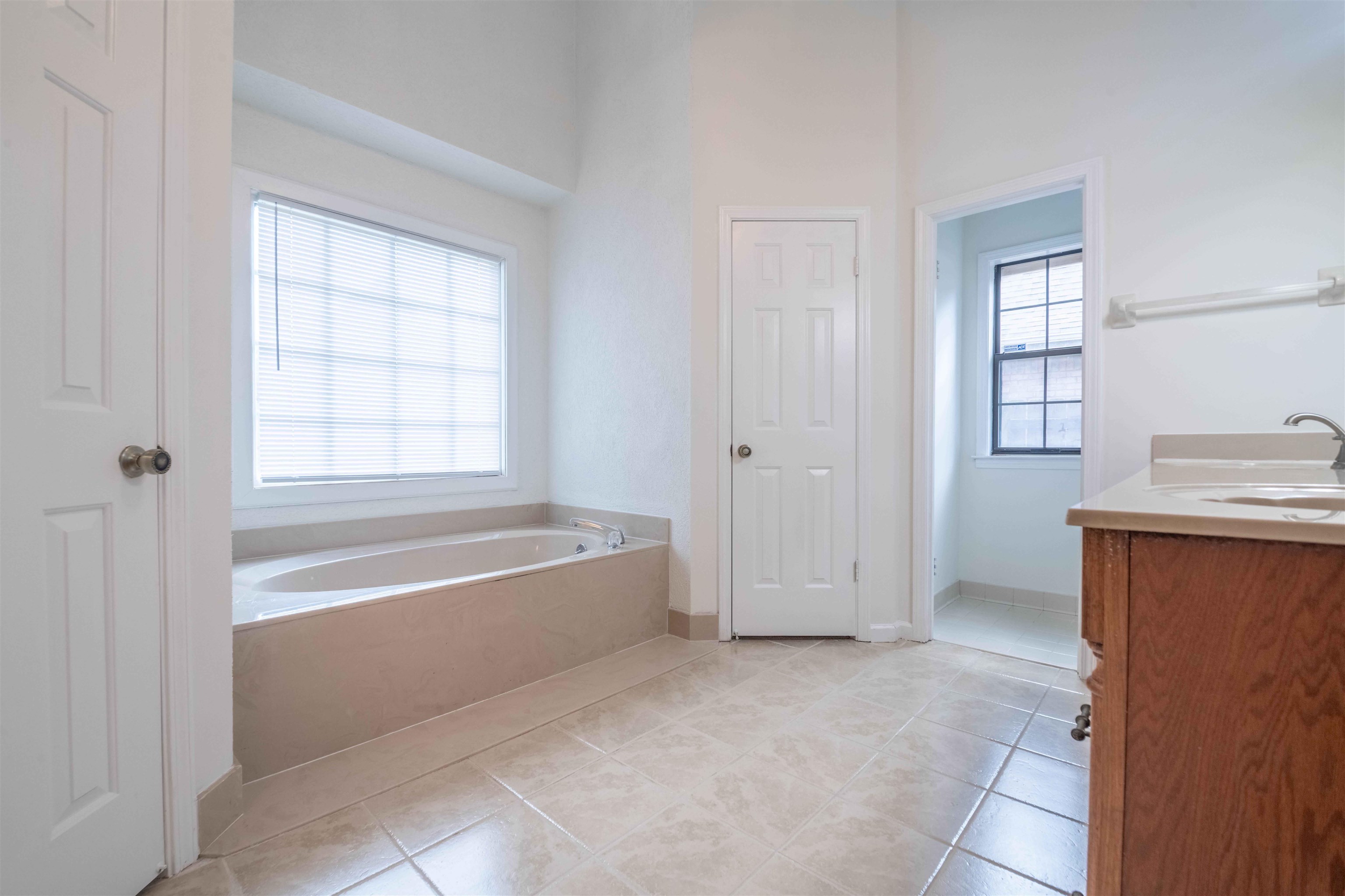 7800 Buck Ridge Cove Memphis, TN 38016 - Photo 23 of 36 Bathroom featuring a built-in soaking tub beneath a window with horizontal blinds, tile flooring, and a wood-finish vanity with a single sink