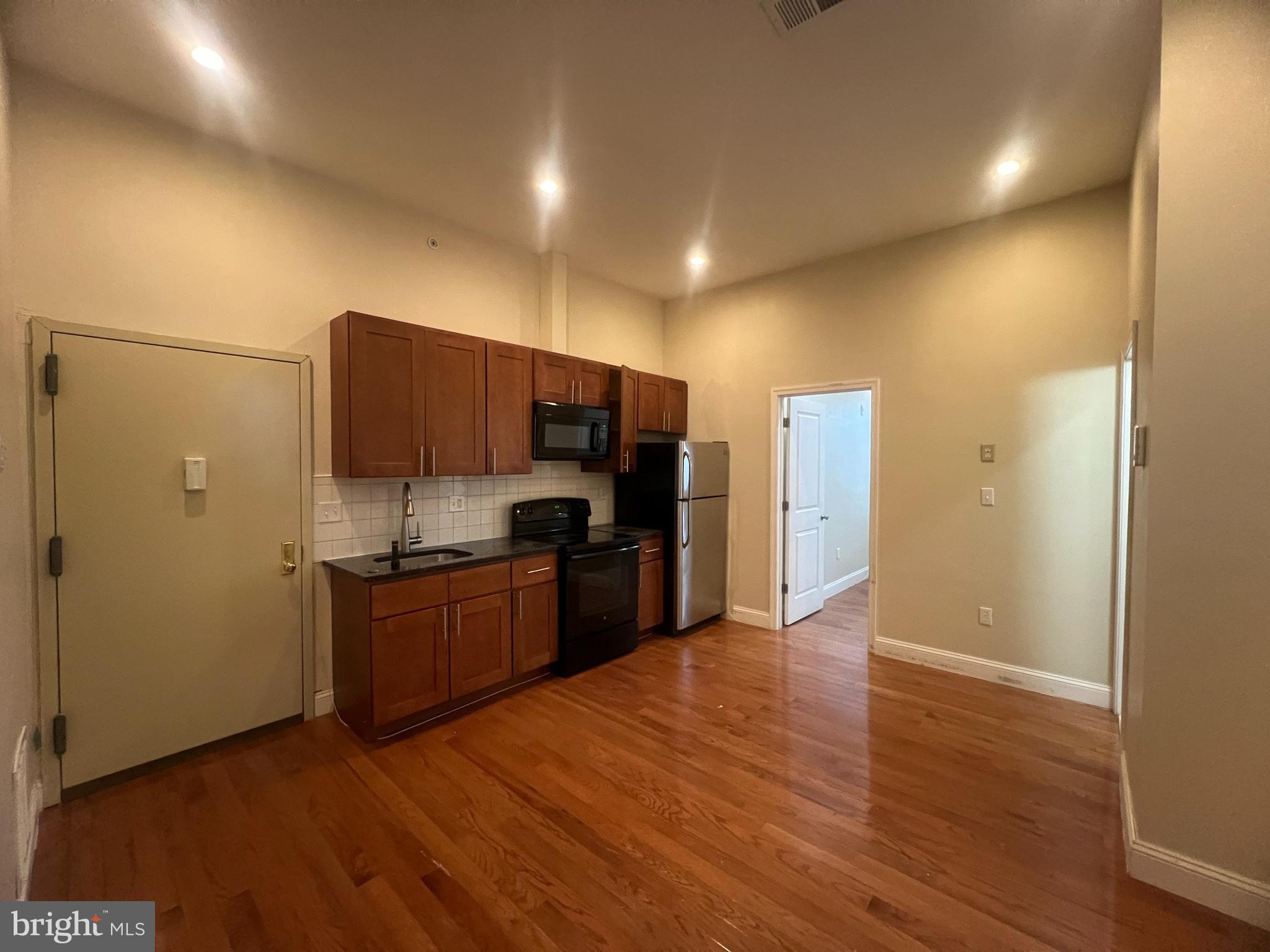 4706 Chestnut Street, Unit 4B Philadelphia, PA 19139 - Photo 1 of 7 a kitchen with stainless steel appliances wooden floors and wooden cabinets