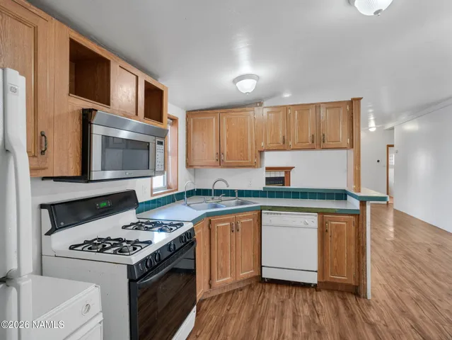 a kitchen with granite countertop a stove top oven a sink dishwasher and white cabinets with wooden floor