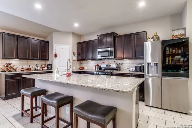 a kitchen with stainless steel appliances granite countertop a stove top oven a sink dishwasher a dining table and chairs with wooden cabinets