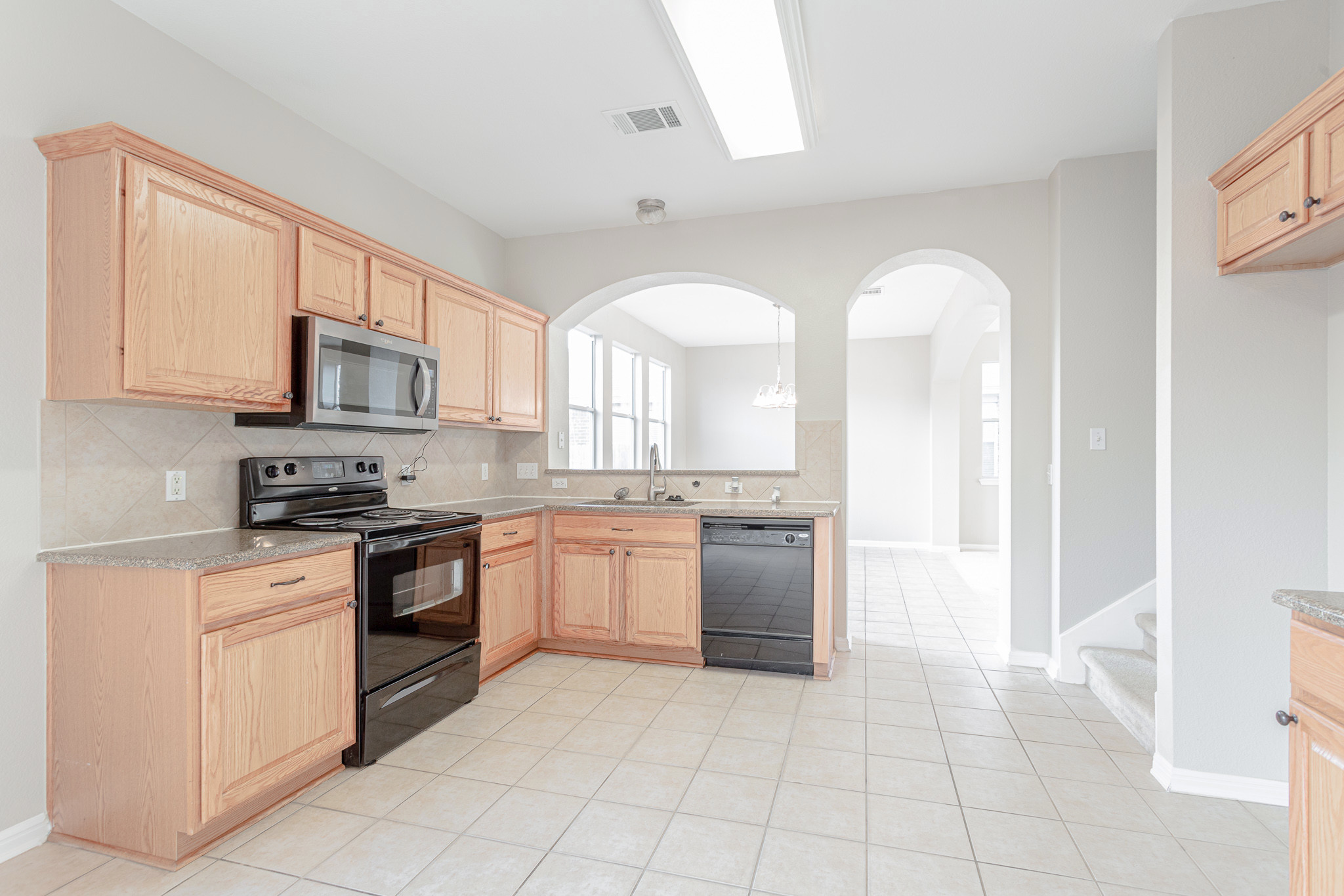 19201 Mangan Way Pflugerville, TX 78660 - Photo 4 of 29 Kitchen with backsplash, black appliances, arched walkways, light brown cabinetry, and light tile patterned floors