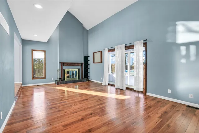 a view of an empty room with wooden floor fireplace and a window