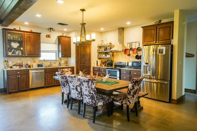 a kitchen with stainless steel appliances a dining table chairs refrigerator and sink