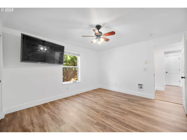 a view of an empty room with wooden floor and a ceiling fan