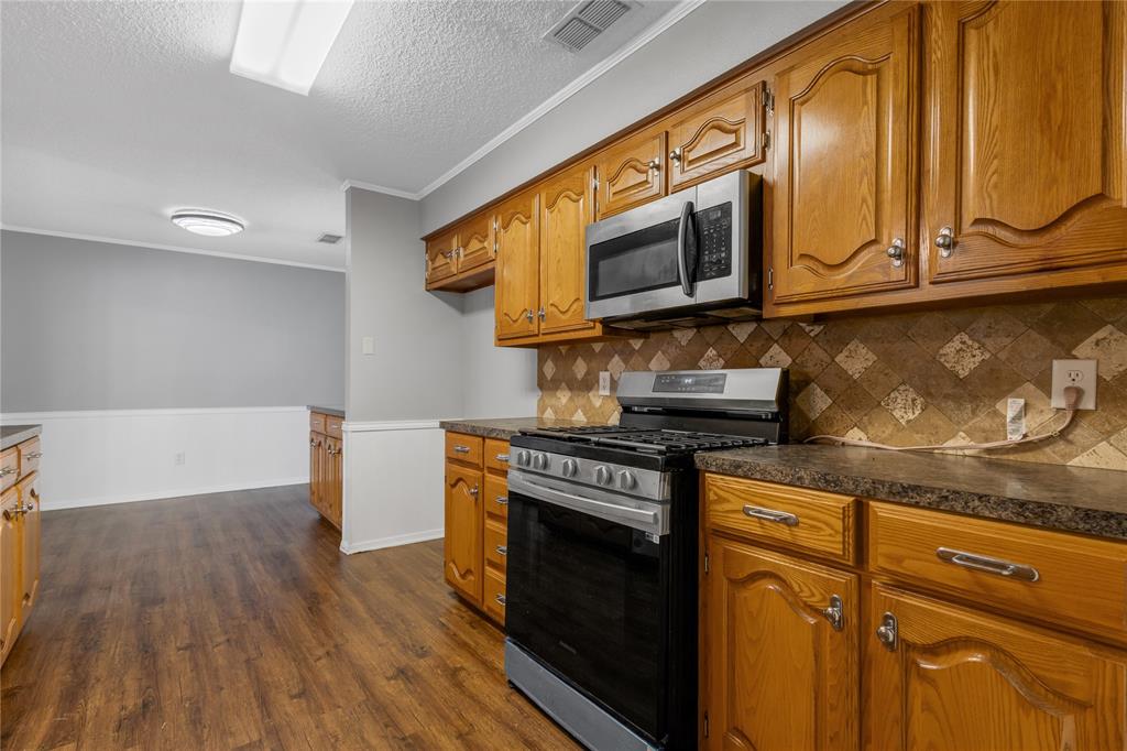 1609 Robin Street Mineola, TX 75773 - Photo 5 of 24 Kitchen featuring wood cabinetry, stainless steel microwave, gas range, patterned tile backsplash, and dark countertops