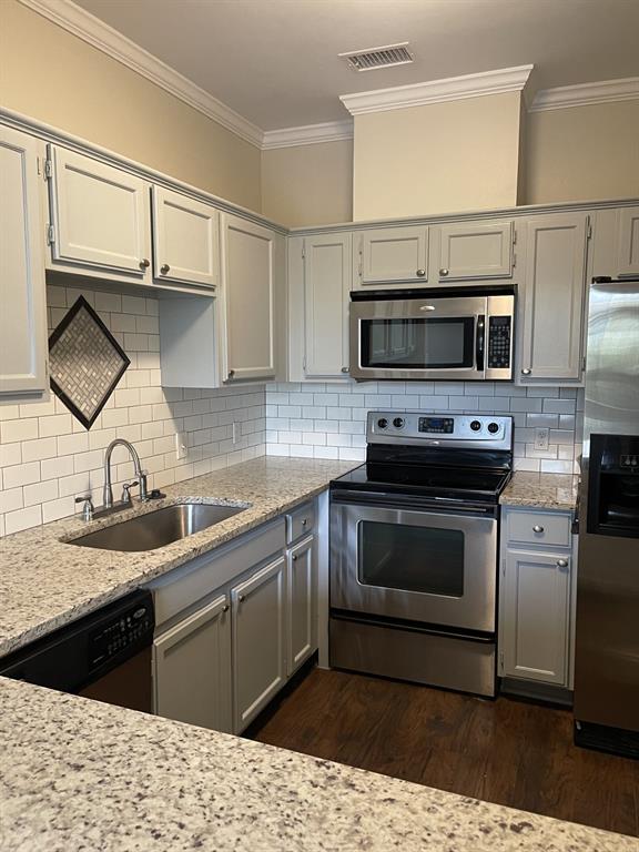 5310 Keller Springs Road, Unit 423 Dallas, TX 75248 - Photo 3 of 7 Kitchen featuring stainless steel appliances, gray cabinetry, light stone counters, ornamental molding, and dark wood finished floors