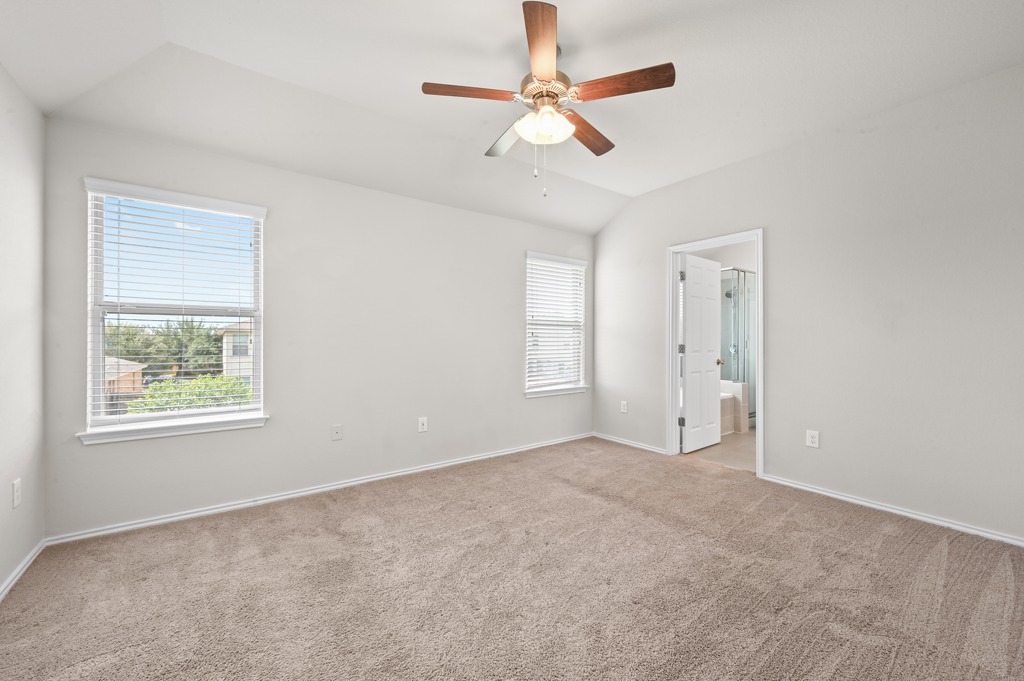209 Noddy Road Buda, TX 78610 - Photo 17 of 27 Plush carpeting and a vaulted ceiling elevate this comfortable primary bedroom retreat.