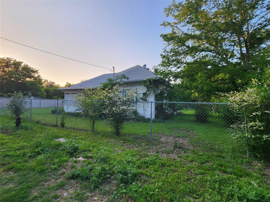 403 Barker Street Cumby, TX 75433 - Photo 1 of 16 Grassy yard space featuring a chain-link fence, mature trees, and established bushes