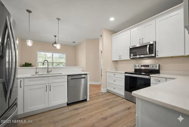 a kitchen with stainless steel appliances white cabinets a sink a stove a refrigerator and microwave