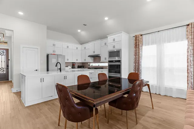 a kitchen with stainless steel appliances granite countertop a dining table chairs a refrigerator and cabinets