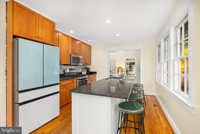 a kitchen with granite countertop stainless steel appliances a refrigerator a stove a sink a dining table and chairs with wooden floor