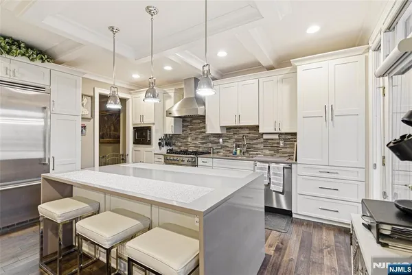 a large white kitchen with a refrigerator a stove a sink and a dining table with wooden floor