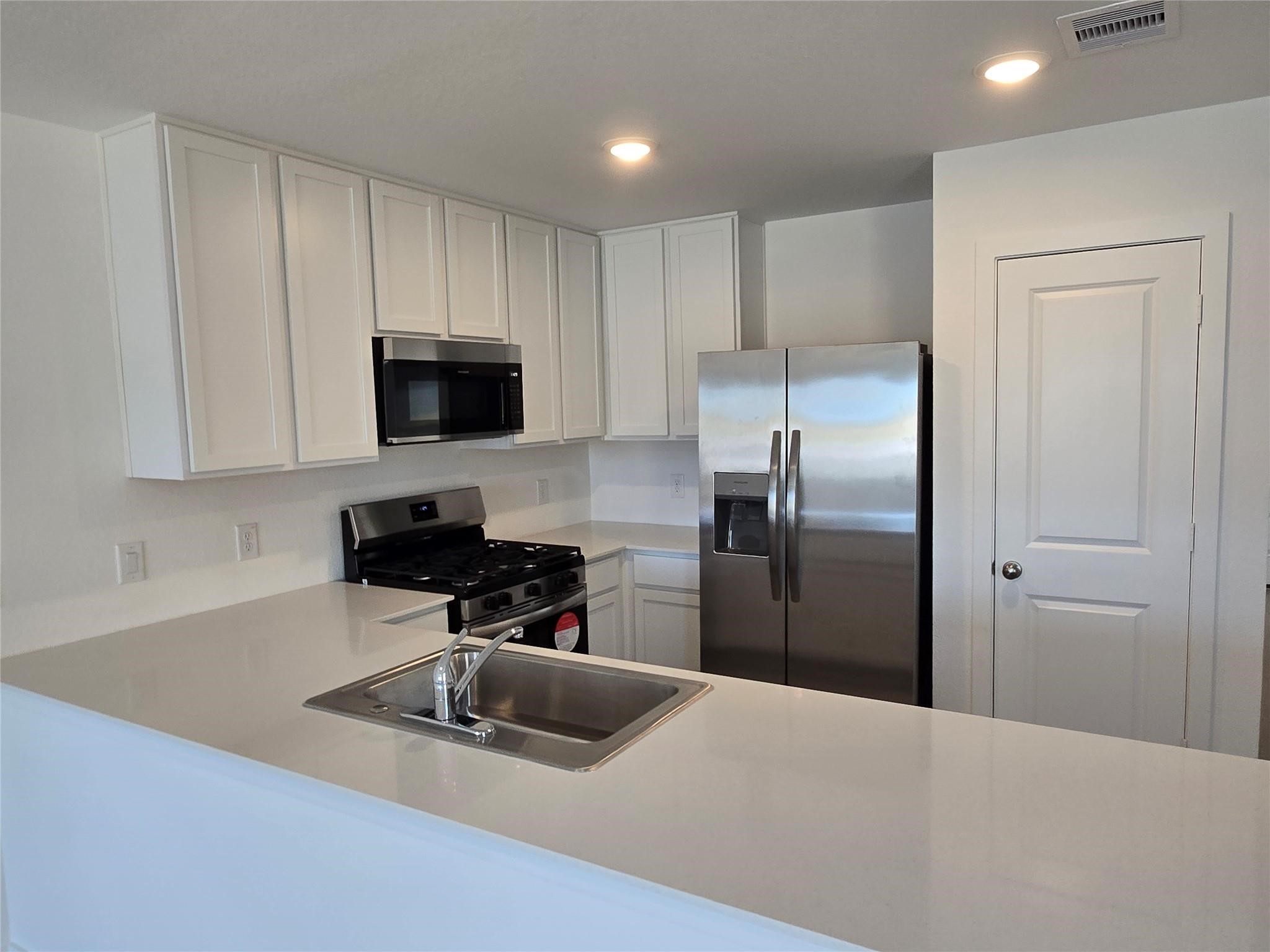 658 Maria Elena Way Cleveland, TX 77327 - Photo 3 of 24 a kitchen with a refrigerator a microwave a sink and a stove