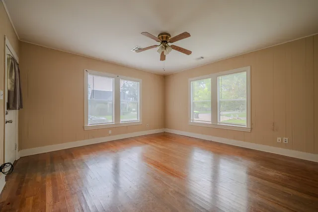 a view of a livingroom with a hardwood floor a ceiling fan and windows