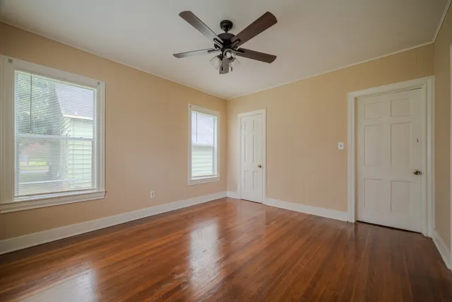 an empty room with wooden floor chandelier fan and windows