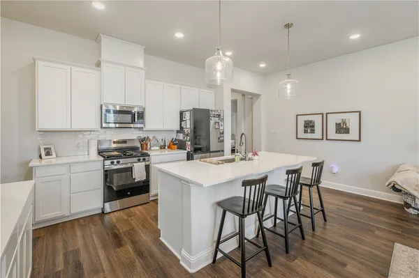 a kitchen with stainless steel appliances kitchen island granite countertop a stove a sink a microwave a refrigerator and white cabinets with wooden floor