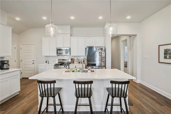 a kitchen with stainless steel appliances kitchen island granite countertop a stove a sink a microwave a refrigerator and white cabinets with wooden floor