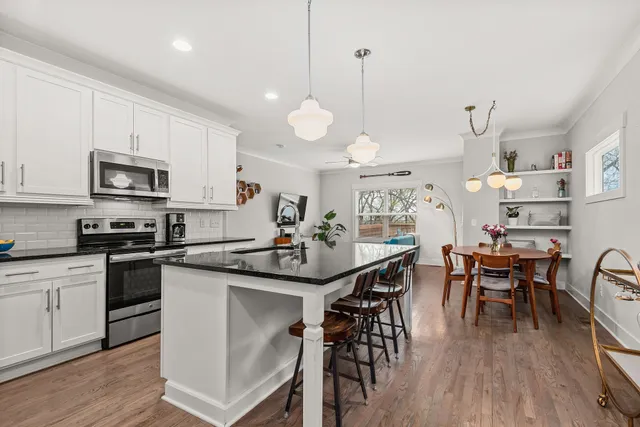 a kitchen with stainless steel appliances kitchen island granite countertop a stove top oven a sink a dining table and chairs with wooden floor