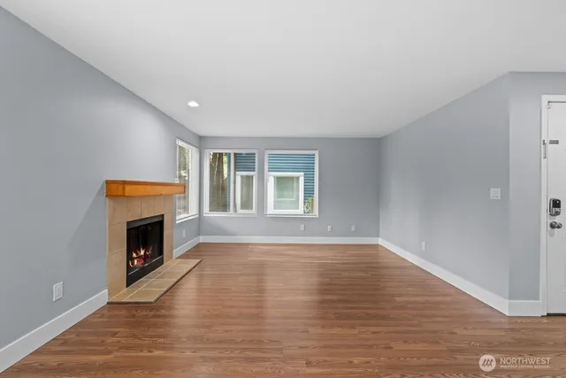 a view of an empty room with wooden floor fireplace and a window