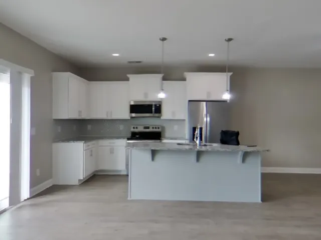 a kitchen with stainless steel appliances a sink a stove a microwave a refrigerator a white cabinets and wooden floor