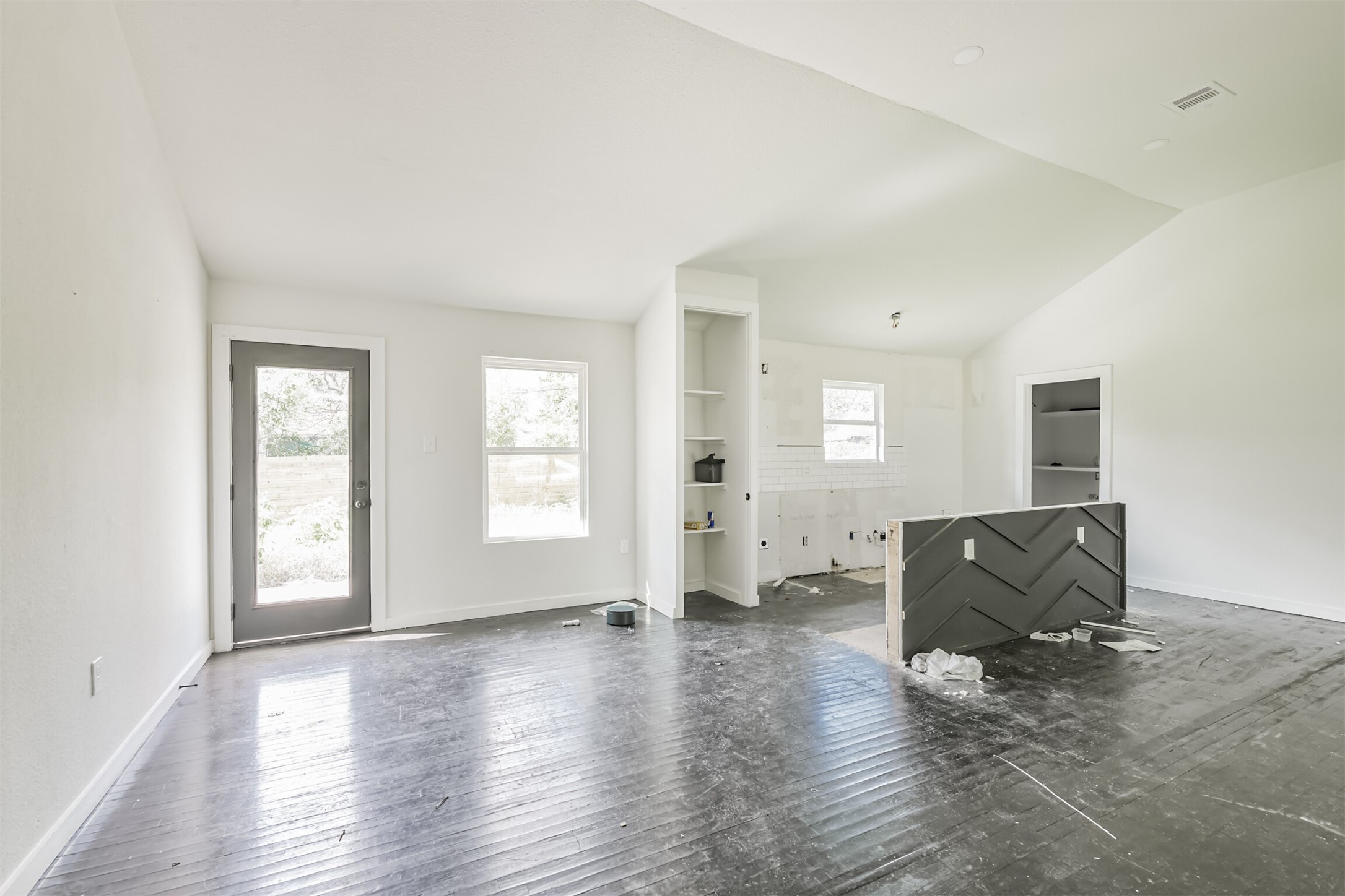 209 Leago Street Houston, TX 77022 - Photo 7 of 24 This photo shows a bright, open-concept living space with unfinished flooring and a partially completed kitchen area. Large windows and a glass door allow natural light to fill the room. Ideal for customization and personalization.