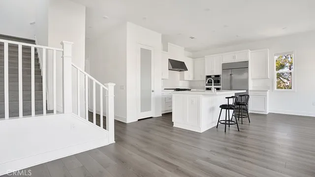 a kitchen with stainless steel appliances granite countertop a stove top oven a sink a refrigerator white cabinets and wooden floor