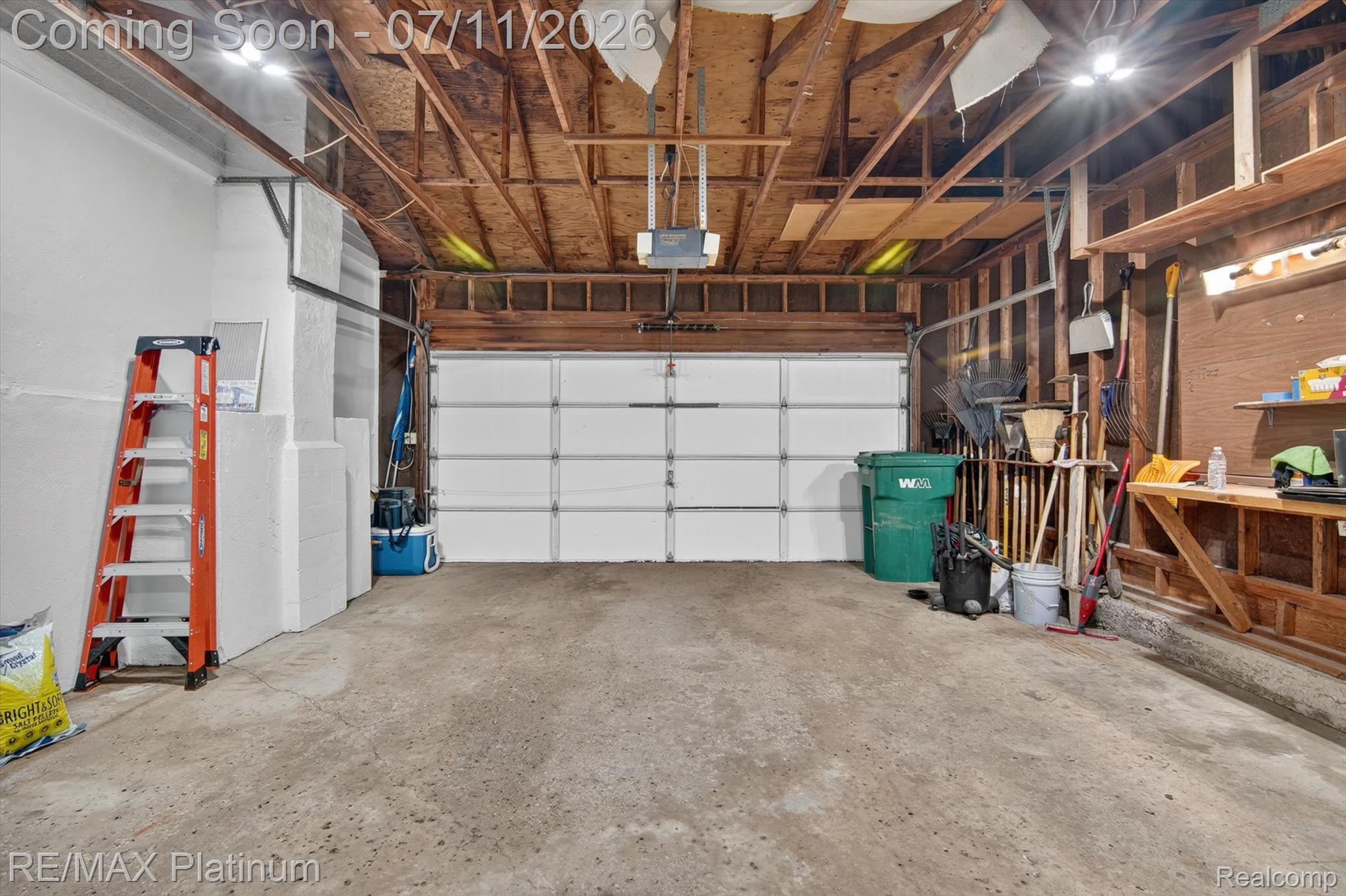 13365 North Territorial Road Gregory, MI 48137 - Photo 39 of 52 Garage interior featuring a sectional white overhead door, exposed wood beam ceiling, concrete flooring, and built-in shelving