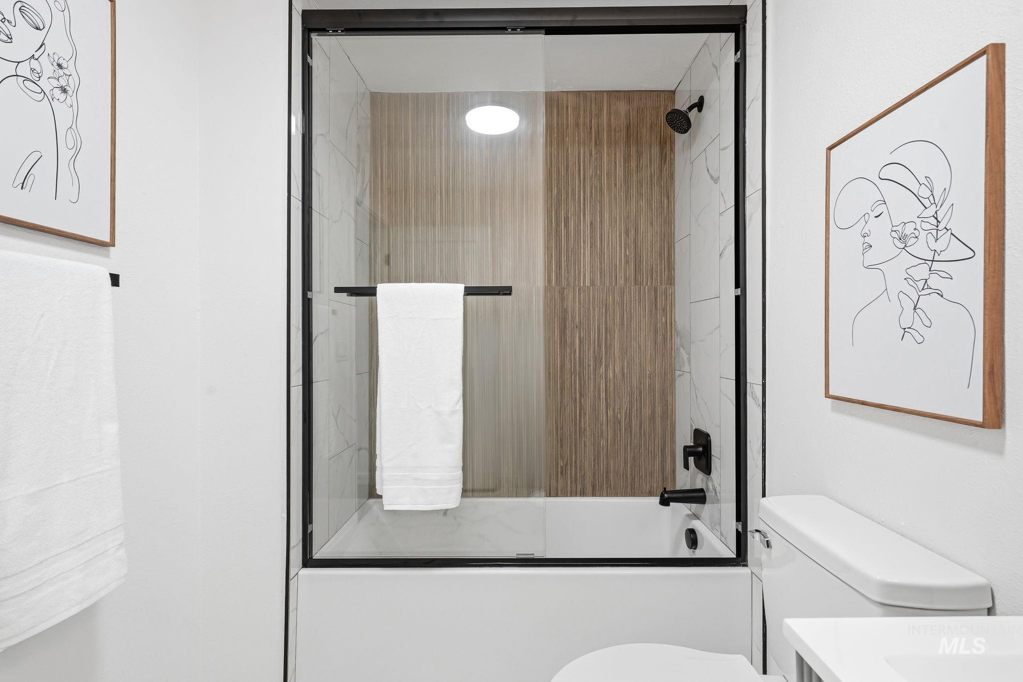 2152 Artesian Road Eagle, ID 83616 - Photo 28 of 50 Bathtub with sliding glass enclosure featuring matte black hardware, white subway tile surround, and vertical wood-finish accent tiling